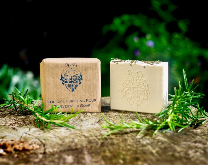 2 Louisa's Purifying Four Thieves Milk Soaps one wrapped in brown paper and one unwrapped on a stone slab with pieces of rosemary either side of the soaps