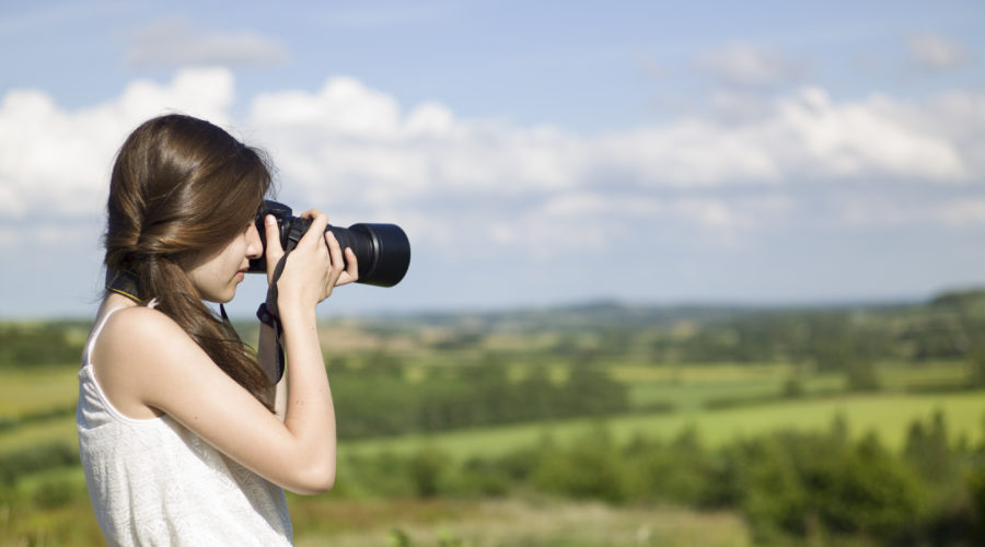 Women in white dress and with long brown hair taking a photo outside with a long-lense camera. Background behind the women features the Lincolnshire Wolds.